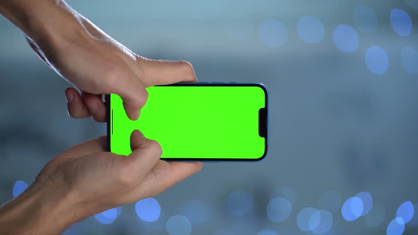 Close-up Of Phone With Green Mock-up Screen In Men's Hands Against Blurred Lights. Man Performing Swipe, Scroll, and Tap Gestures to Smartphone Display | Shutterstock HD Video #1111640793