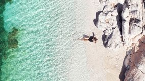4K drone footage of woman dressed black swimsuit prostrated on white pebble beach lying down on the calm Ionian sea waves. Exotic tropical summer holidays concept. Cephalonia island, Greece.