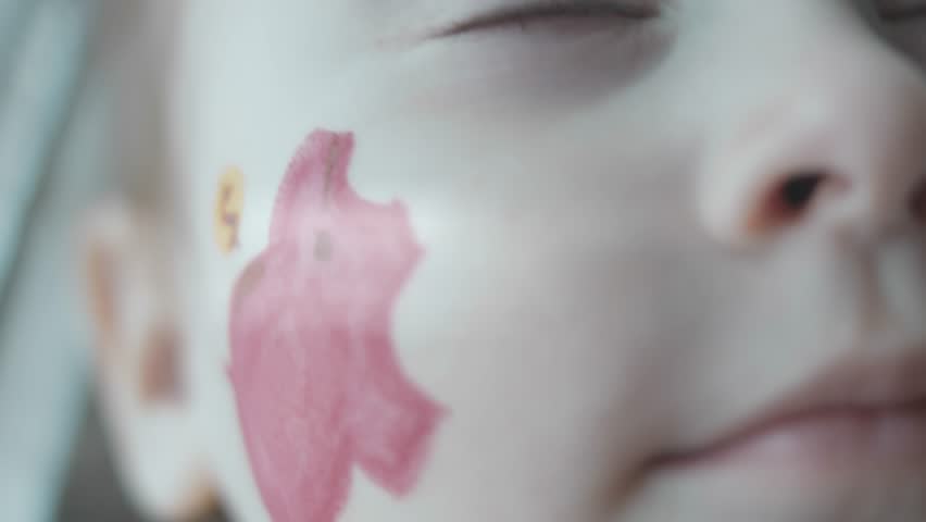 Piggy bank painting on the face of a cute toddler girl. Banking, financial education and deposit concept. Slowmotion