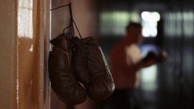 The shot shows a close up of a doorjamb with a rusty nail nailed to it on which boxing gloves hang. In the background a man in boxing gloves stands in a rack and hones his punches before a fight. - Powered by Shutterstock - Get 15% off with code: PIKWIZARD15