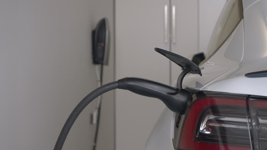 CLOSE UP: Female driver unplugs white electric car while charging in home garage. She disconnects black cord before sitting in the vehicle. Effortless system for recharging engine battery of a BEV. | Shutterstock HD Video #1111650211