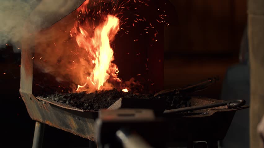 Blacksmith heats a metal product in a furnace for further processing on an anvil in a workshop. Blacksmith hardens steel at high temperature in a homemade furnace in the village