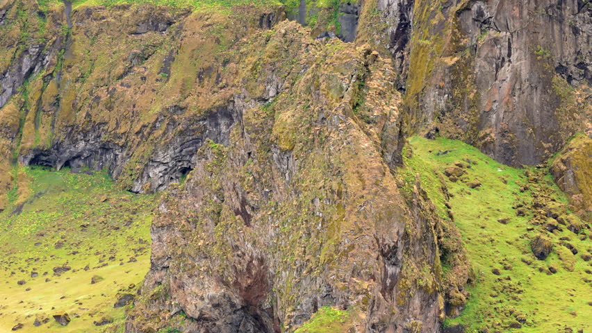 Aerial view of giant volcanic rocks of wonderful shapes blanketed with moss of different shades of green, creating a long wall of mountains with lowlands. High quality 4k footage Royalty-Free Stock Footage #1111652269