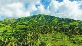 Scenic summer landscape of mountain peaks in front of a cloudy sky. Mountain valley in the morning sun. Vibrant tropical nature of the Dominican Republic. Multi-colored hills with green meadow grass.