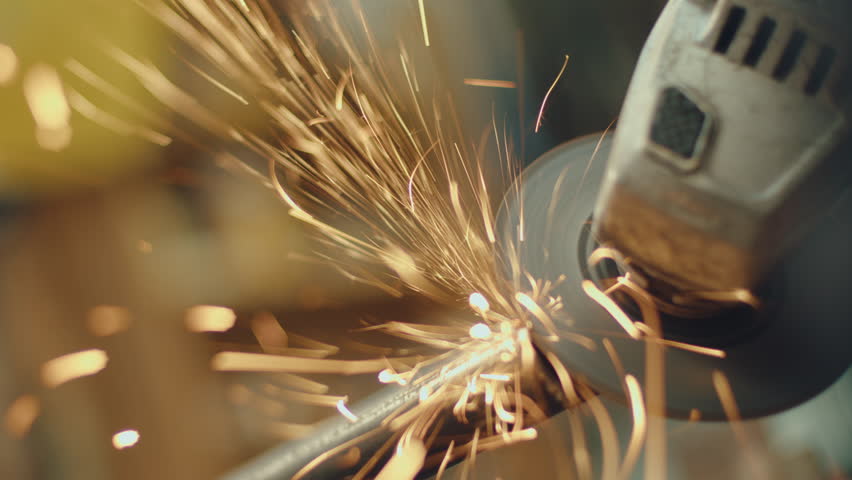 Hands of unrecognizable industrial worker cutting steel pipe with disk grinder, sparks flying around during metalwork. Close-up shot, dutch angle