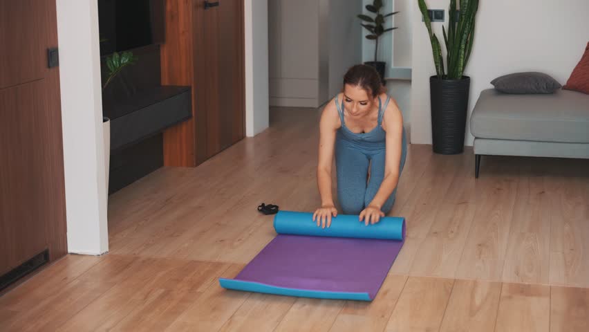 Young happy woman hands rolls up folds carpet mat cleans up after training at home. sportswear suit blue top leggings. living room  modern trendy interior. aerobics sport fit yoga workout fitness 4k | Shutterstock HD Video #1111662177