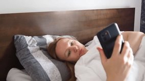 A woman using smart phone lying in bed late at morning or night. Typing a message on the phone, social networks, playing games, watching videos online, scrolling screen. people's screen addiction.