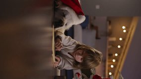 Young boy and his dog lying near Christmas tree and writing letters to Santa Claus. Joy and traditions of Xmas. Boy consults with dog, whispers in its ear. Vertical cinematic video, advertisement.
