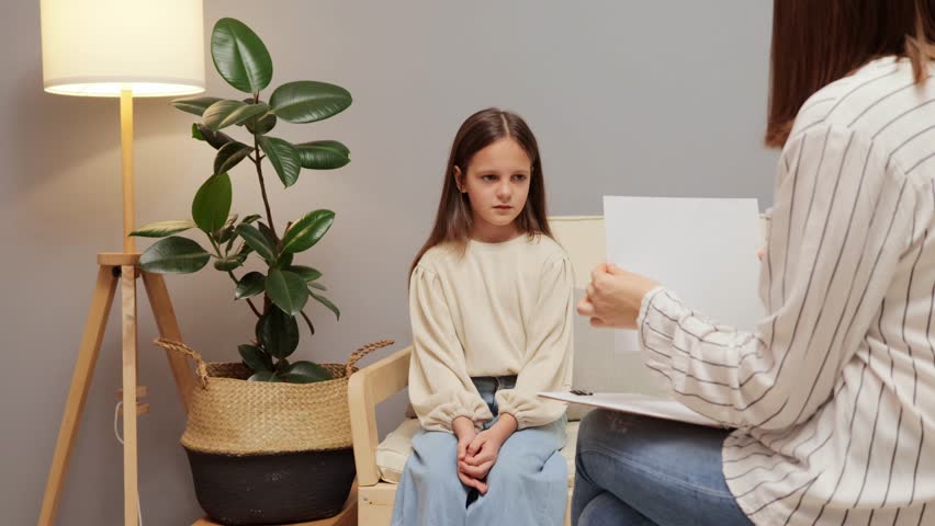 Kid's counseling session. Child's emotional comfort. School psychologist discussion. Therapist's empathy talk. Child psychologist showing picture to little smart girl doing psychological test. Royalty-Free Stock Footage #1111672319