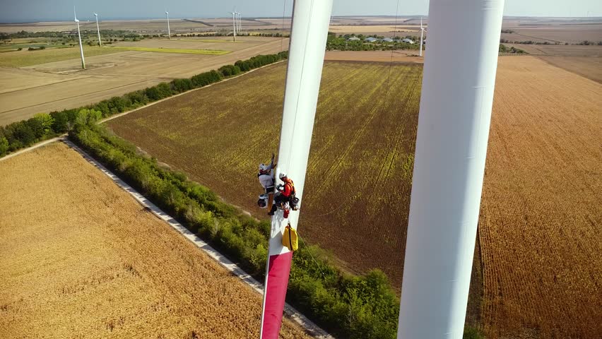 Aerial high angle shot of technicians repairing a wind turbine generator blade. Industrial Rope Access workers descending to grind and repair fiberglass edge of wind turbine. Work at height. Abseiling Royalty-Free Stock Footage #1111672907
