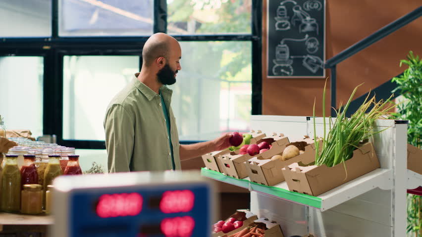 Man examining organic pantry supplies stored in reusable glass jars, looking to buy ecological products from sustainable local store. Bio supermarket with natural healthy food, vegan lifestyle.