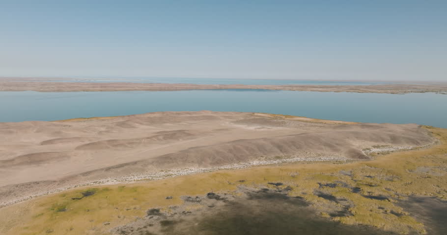 Coast Lake Balkhash, Kazakhstan. Beautiful turquoise color with sky reflections and white wave. Rocky sand shore with yellow arid dry grass and saline. High altitude drone view at summer sunny day.