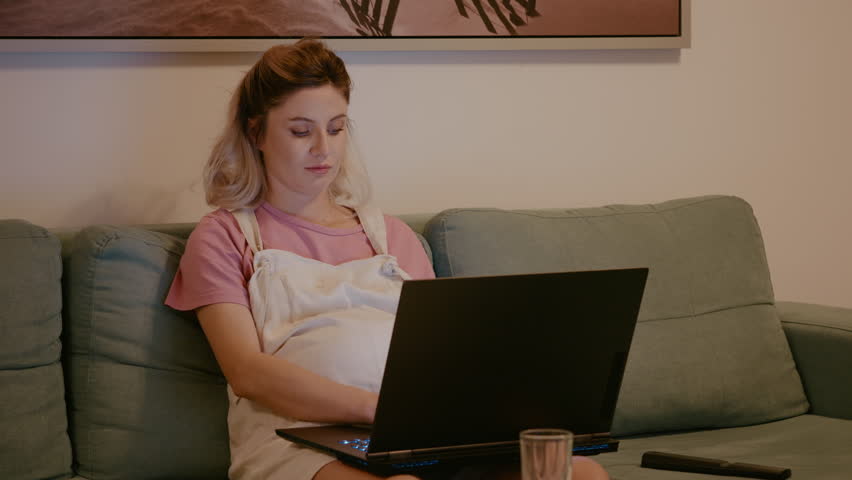 Concentrated pregnant feeling baby kicks while remotely working. Pregnant employee designing presentation and marketing strategy while on maternity leave. | Shutterstock HD Video #1111680825