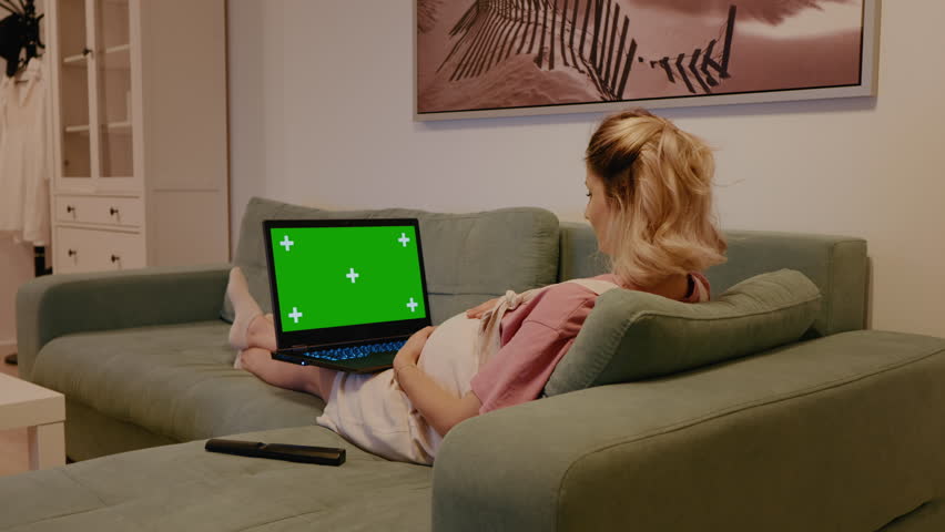 Zoom in pregnant having conference while on maternity. Relaxing on sofa mom to be while watching chroma key laptop. | Shutterstock HD Video #1111680829
