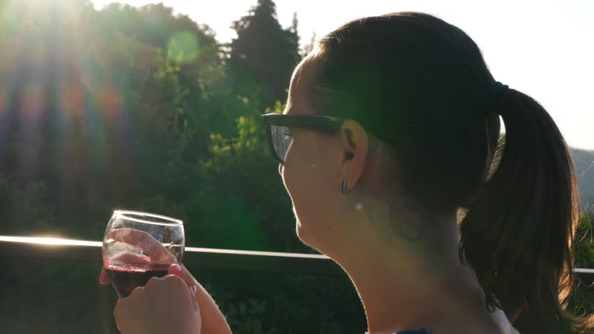 Close-up of pretty woman in sungalsses drinking red wine on a terrace and enjoying view of summer nature, slow motion