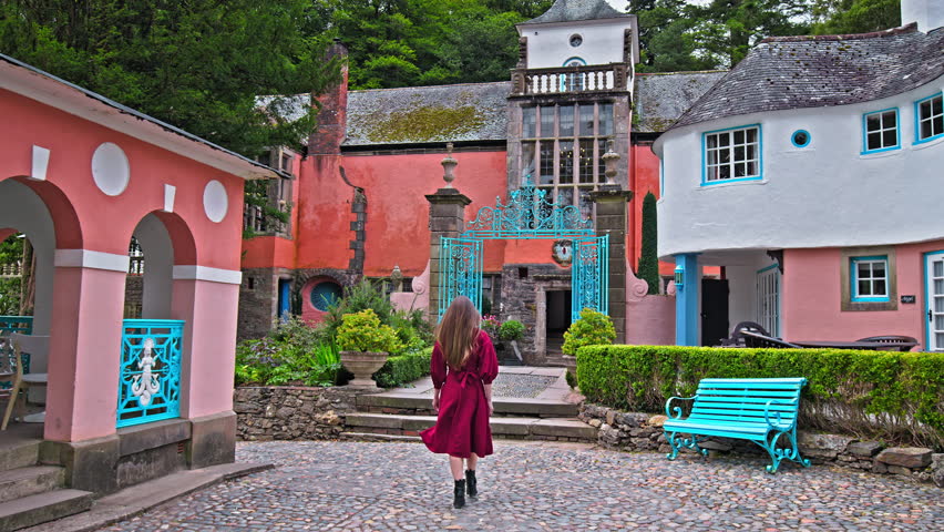 A beautiful girl in a red dress visits Portmeirion village. Female tourists enjoy the view of the beautiful coloured houses and gardens in Gwynedd, North Wales.