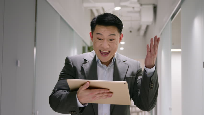 Happy excited middle-aged Asian businessman chinese korean japanese man with digital tablet win business success bet money lottery amazed 40s male winning financial prize achievement at office hall | Shutterstock HD Video #1111694341