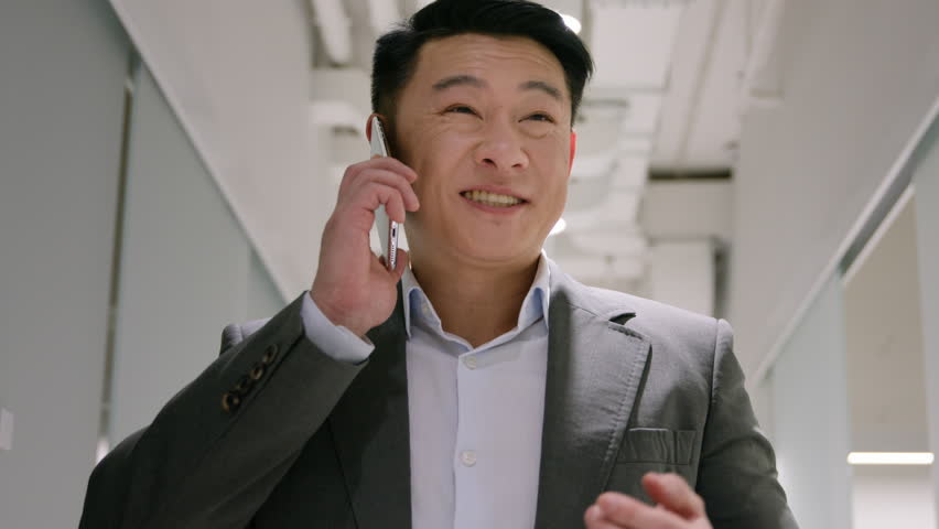 Happy Asian businessman chinese japanese ethnic man calling mobile phone in modern office hallway male joyful employer business manager answer smartphone call discuss converse negotiate communicate | Shutterstock HD Video #1111694345