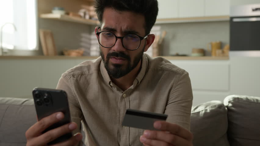 Stressed Arabian Indian man frustrated upset male cardholder pay online service with bank credit card using mobile phone disappointed banking app error no money balance lack finances financial limit | Shutterstock HD Video #1111694347