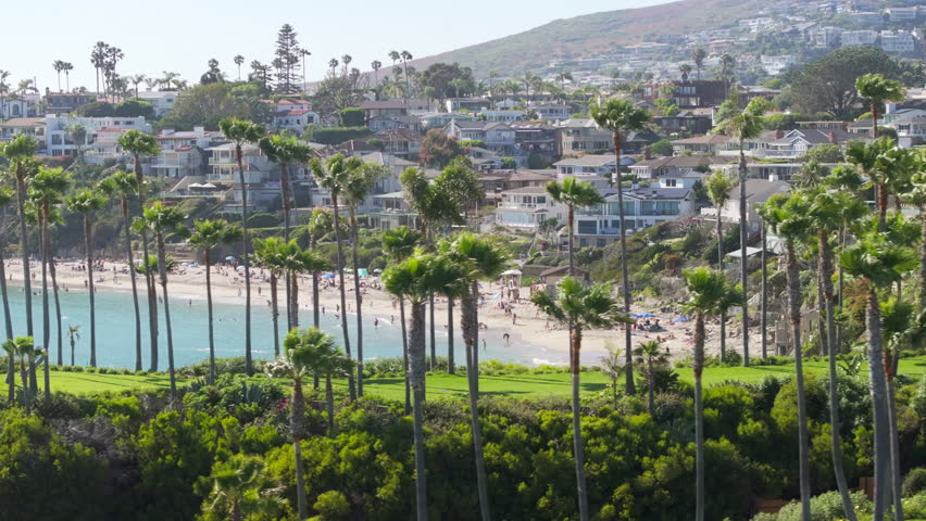 Panoramic view of resort town - Laguna beach with stunning ocean landscape, Orange County, California, USA. People chilling on the beach. Landscape with tall palm trees and mountains at Pacific Ocean