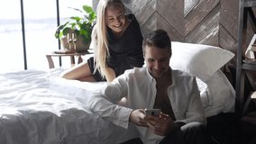 A girl with a smile hugs her lover while he watches funny videos on the phone.