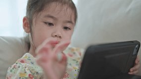 Asian child girl using pen and touch drawing on tablet display screen. Baby smiling funny time to use tablet. Too much screen time. Cute girl watching videos while tv, Internet addiction concept.