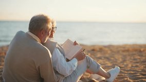 Senior gray haired man woman reading book together sitting on sandy sea beach at sunset in evening. Happy marriage, old family spending enjoy time. Love couple relationship, leisure, resting concept. - Powered by Shutterstock - Get 15% off with code: PIKWIZARD15