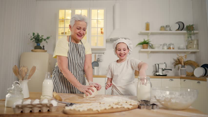 Happy family, granny and granddaughter cook together in kitchen. They make cookies star shape from dough. Homemade bakery, sweets, pastry concept. Smiling pre-teen girl wears cook