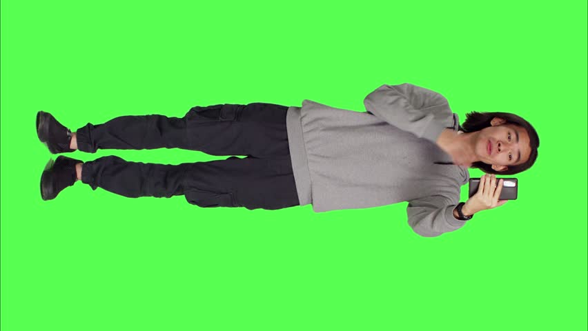 Front view of asian person on videocall network with friends, using smartphone to call friends using phone camera against greenscreen. Male adult talking to people on videoconference connection.