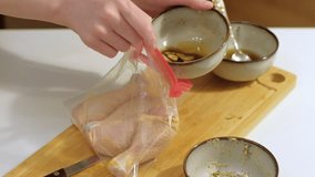 Preparing and marinating raw chicken meat, spicing and packing in plastic bag. Female hands. Fresh chicken meat on wooden chopping board. Cooking healthy food concept. High quality FullHD footage