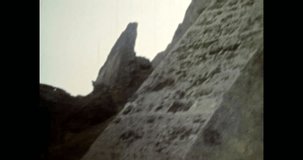 Sheer impregnable fortress wall in sunset sunlight. Medieval defensive castle bastion outside exterior. Down-up epic view of historic landmark. Vintage footage of overscan archival film. 1980s archive