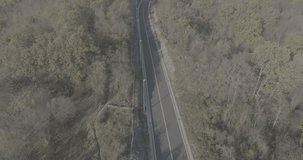 Aerial video over the highway in autumn forest. Nice landscape with beautiful colors of the trees. Car passing on the road.
