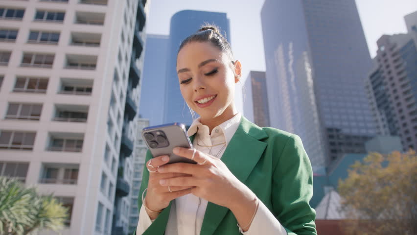 Young stylish elegant successful beautiful business woman using smart phone outside. Happy professional businesswoman executive holding cellphone modern tech standing at urban city street background