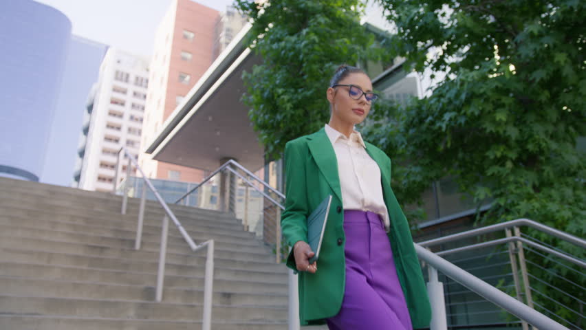 Thoughtful woman looking away outdoors at modern city. Smart young lady boss in fashionable blazer at downtown street. Portrait confident businesswoman walking down the stairs in stylish suit outdoors