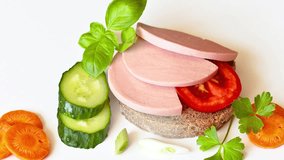 Video of appetizing sandwich with boiled sausage and vegetables: tomato, cucumber, carrots and basil for breakfast. White background, closeup