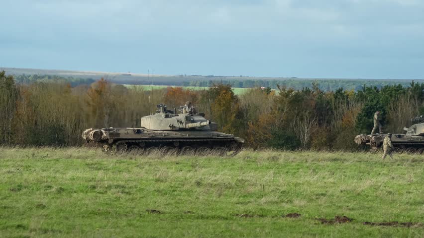 a British army Challenger II 2 FV4034 main battle tank following a guide soldier to a stop amongst a squadron of parked tanks  