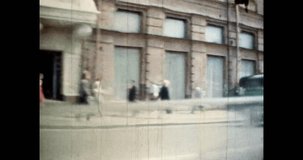 Traveling by car through city center in sunny summer. Busy city life. Rush people walk along street. Urban historical architecture view from moving car. Retro archival film. 1980s vintage archive 