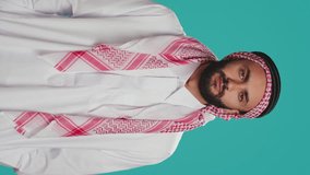 Vertical video Muslim guy nodding in studio shot, saying yes and expressing his approval. Arab person in traditional clothes showing support about something. Middle eastern man doing positivity and