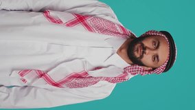 Vertical video Arab person poses with fingers crossed and praying to allah over blank background, showcasing religion and spiritual devotion. Man in muslim clothes being religious, worshipping God