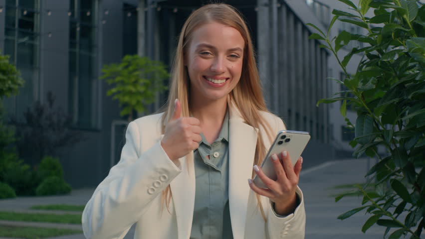 Caucasian woman girl female businesswoman business lady checking email message using phone outdoors reading good news on smartphone showing thumbs up gesture approval agreement sign excellent result | Shutterstock HD Video #1111751073