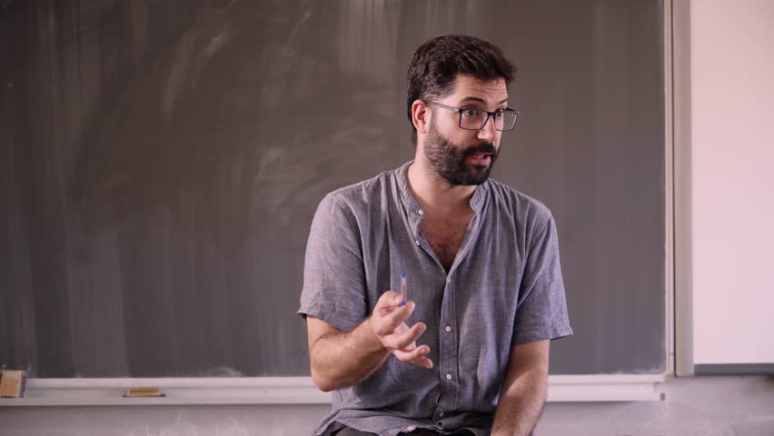 Group tutor gives informal informative talk to several teenage students of his subject. Vocational students listen to the teacher. People inside the classroom.