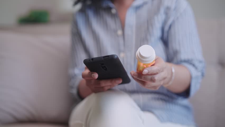 Asian midlife woman using her mobile to search for details about the medication she's about to take at home on a relaxing day.