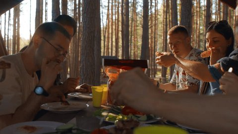 Friends have fun eating in gazebo in nature. Stock footage. Delicious grilled vegetables and meat on table in forest gazebo. Group of friends relax in nature with food in forest Stock video
