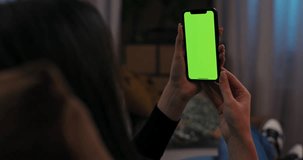 Green mockup screen young female lying on couch holding cell phone smartphone with green screen in hands watching funny video observing different photos videos online surfing internet social media.