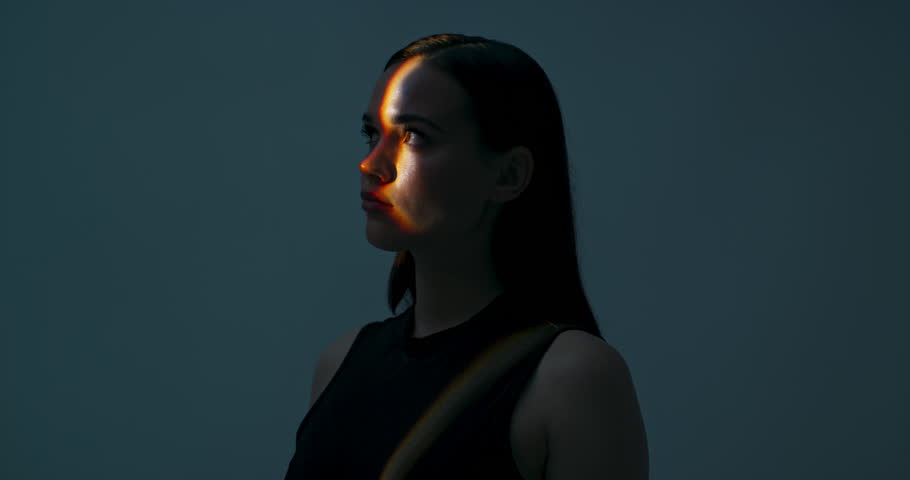 Young female in profile standing in studio isolated in bright light looking up playing with light dansinc with hands. Multicolour future of advertisement concept futuristic time.