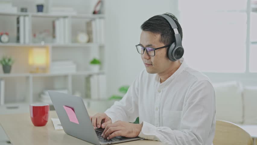 Asian freelance business man wearing headphones making video call in home office, using laptop, talking, watching webinar or studying language, speaking, online training, explaining, e-learning. Royalty-Free Stock Footage #1111765715