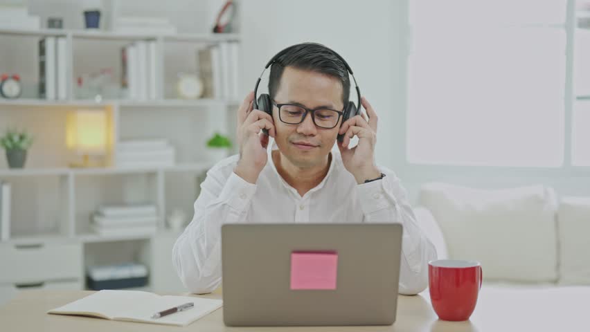 Asian freelance business man wearing headphones making video call in home office, using laptop, talking, watching webinar or studying language, speaking, online training, explaining, e-learning. Royalty-Free Stock Footage #1111765719