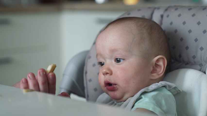 Happy family concept. the child is sitting at table. mother's hand feeds the baby porridge from a spoon. baby with a bib eats while sitting on a high chair. mother feeds baby healthy food from a spoon Royalty-Free Stock Footage #1111766505