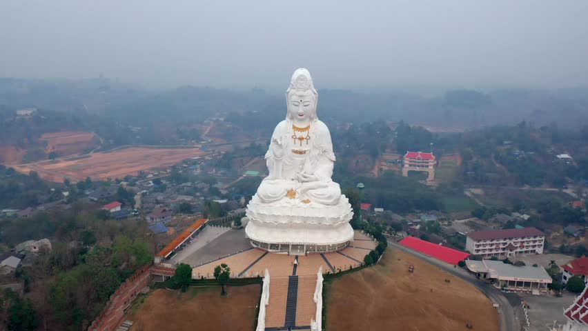 Statue of the goddess of mercy, Guan Yin, in Chiang Rai at Wat Huay Pla Kang. This drone shot circles around the hilltop to reveal all of the surrounds in northern Thailand during burning season. | Shutterstock HD Video #1111769145
