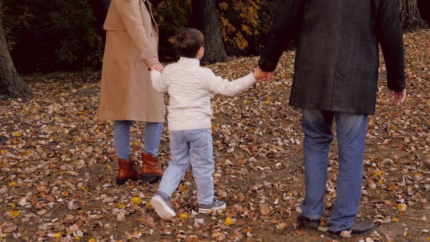 Family relishes afternoon walk in park. Family walking among splendid autumn surroundings takes pleasure in calm stroll. Family strolls on lawn covered with leaves fully immersing in beauty of season | Shutterstock HD Video #1111770109